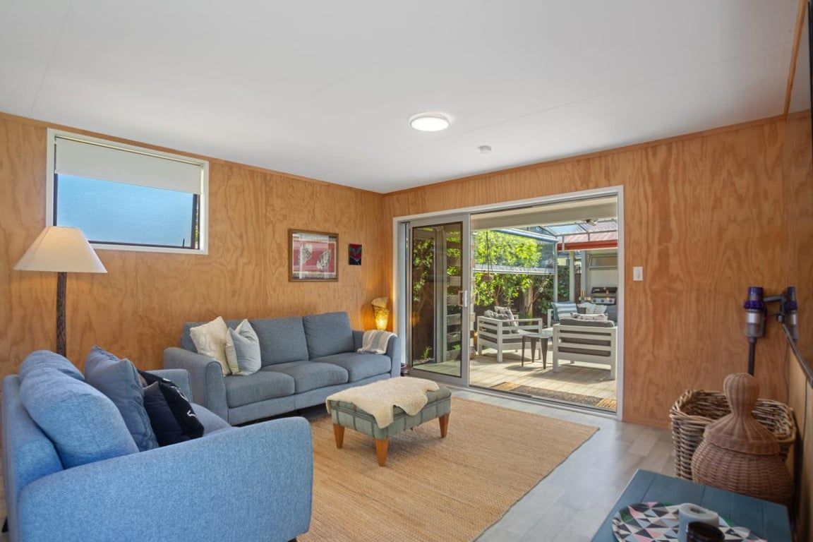 A modern living room with a sofa set, a coffee table, and a large sliding glass door leading to an outdoor patio area.