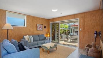 A modern living room with a sofa set, a coffee table, and a large sliding glass door leading to an outdoor patio area.