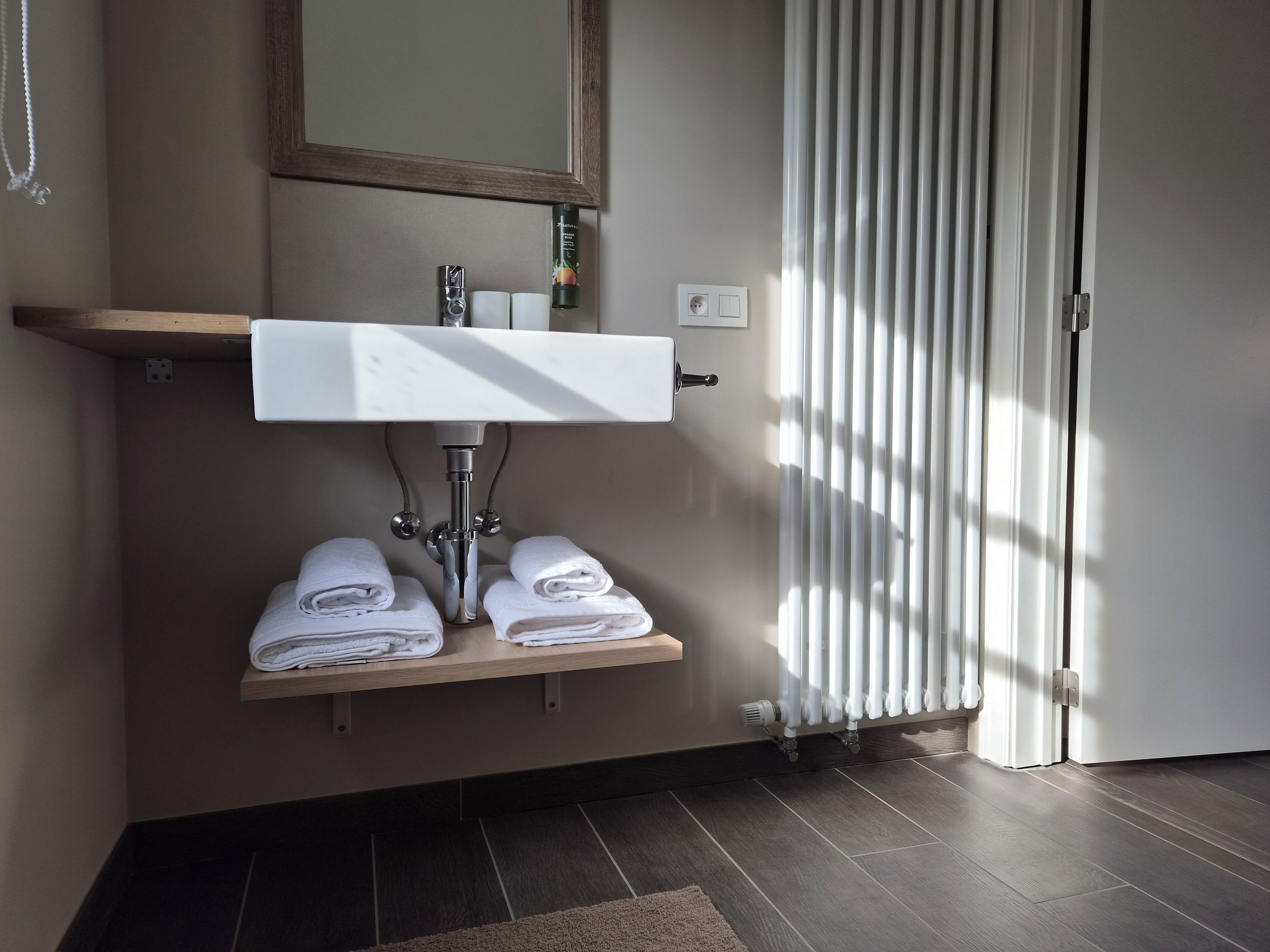 A bathroom with a white sink, two towel racks, a mirror, and a radiator.