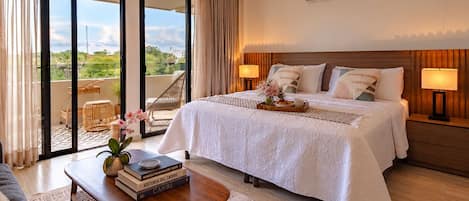 Una habitación de hotel con una cama grande, un balcón con vistas, un escritorio con libros y un aire acondicionado de pared.