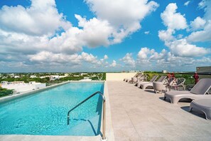 Una piscina en la azotea con agua cristalina, rodeada de sillones de descanso y vistas a la ciudad.