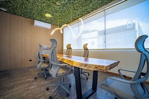 Un salón de conferencias con una mesa de madera, sillas grises, techo verde y un ventanal con vistas.