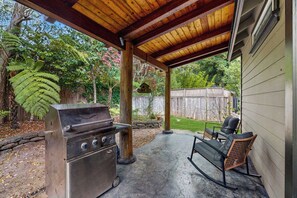 A covered outdoor area with a barbecue grill, a seating area with chairs, and a wooden fence in the background. - Little River Zen - Gardens, BBQ & Pet Friendly (Little River)