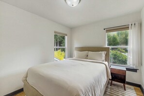 A bedroom with a bed, two windows, a nightstand, and a ceiling light. - Little River Zen - Gardens, BBQ & Pet Friendly (Little River)