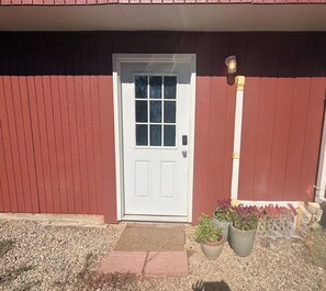 Un edificio rojo con puerta blanca, un pequeño porche y dos macetas.