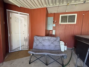 A room with a folding door, a grey cushioned bench, a window, and a water heater.