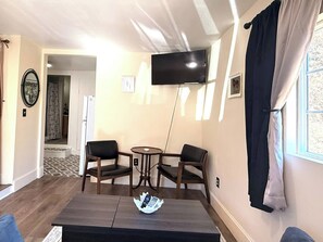 A living room with a TV mounted on the wall, two chairs, a coffee table, and a window with curtains. - Private Pet-Friendly Boise Studio | Hot Tub Access | Near Downtown, Micron & I-84 (Boise)