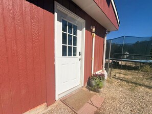 A red building with a white door, a small porch area with a doormat, and a potted plant. - Private Pet-Friendly Boise Studio | Hot Tub Access | Near Downtown, Micron & I-84 (Boise)