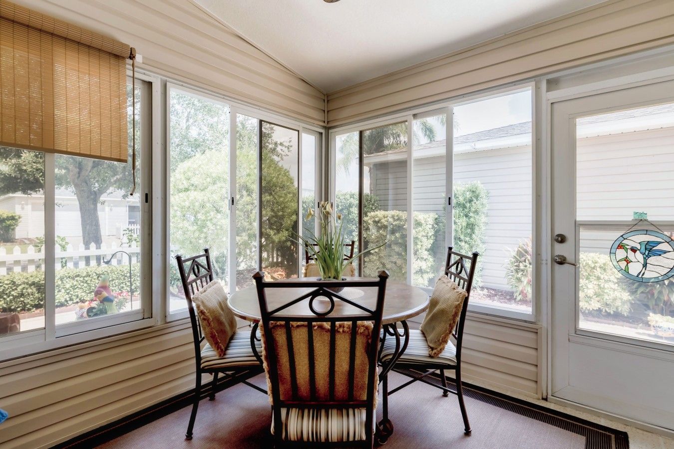 Une véranda avec une table et des chaises, de grandes fenêtres et une vue sur l’extérieur.