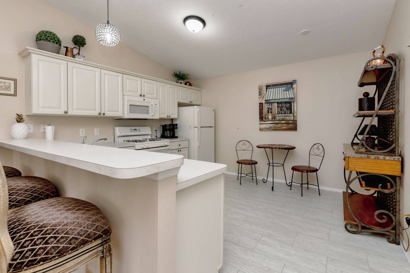 A kitchen with white cabinets, a central island, a dining area with two chairs, and a small table.