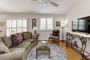 A living room with a sofa, armchair, ottoman, television, and decorative items. - Thurmond Villa Escape in Liberty Park, The Villages (The Villages)