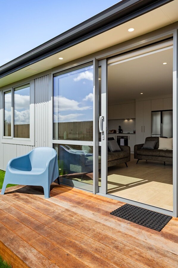 Il s’agit d’une résidence moderne dotée d’une porte-fenêtre coulissante qui donne sur un espace de vie, d’une chaise en plastique bleue à l’extérieur et d’une terrasse en bois.