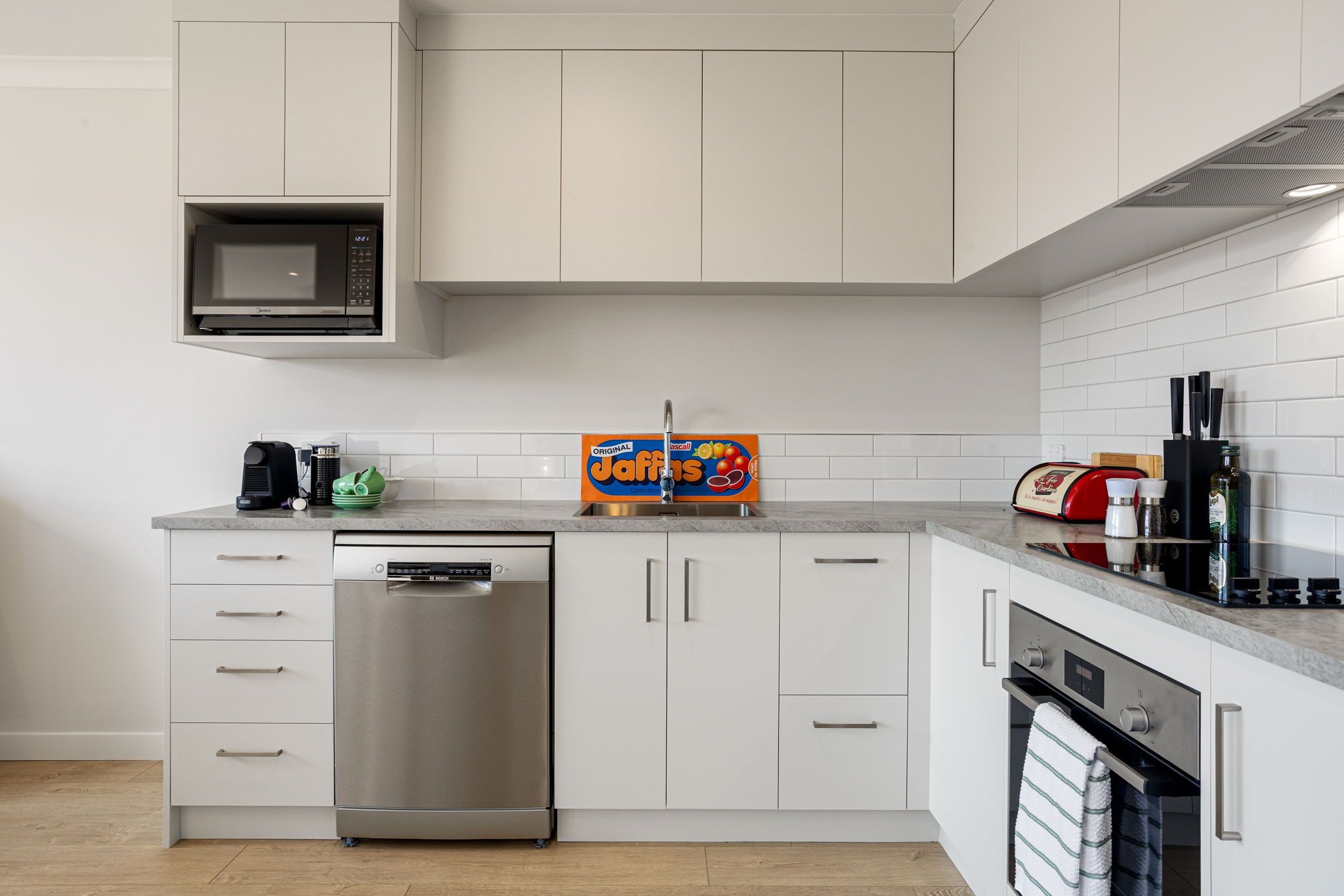 A modern kitchen with white cabinetry, a stainless steel dishwasher, a microwave, and a toaster.