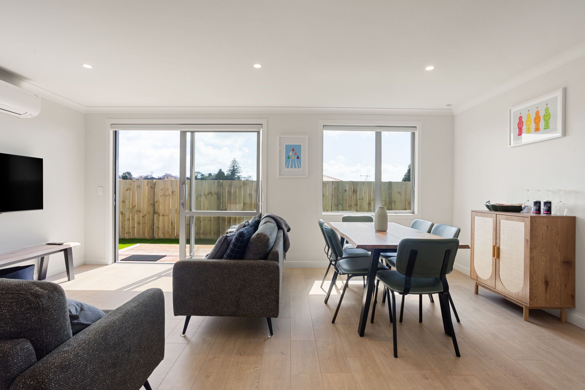 Een moderne woonkamer met een flatscreen televisie, een bank, een eettafel met stoelen en een houten kast.