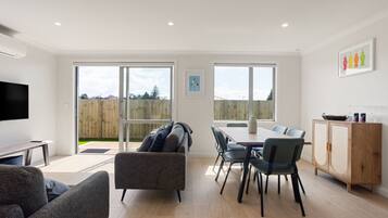Een moderne woonkamer met een flatscreen televisie, een bank, een eettafel met stoelen en een houten kast.