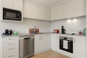 Une cuisine moderne avec des meubles blancs, un lave-vaisselle Bosch, un four à micro-ondes, un grille-pain et un évier.