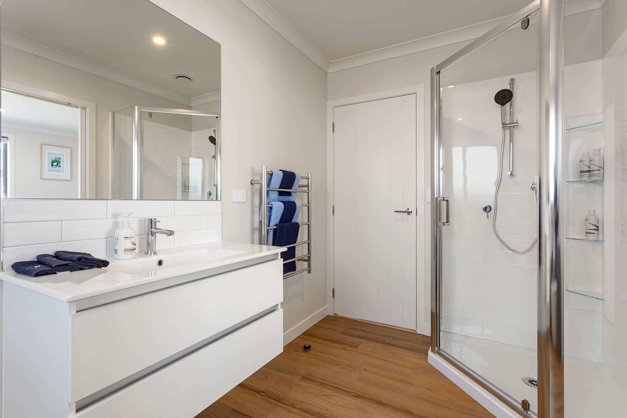 Uma casa de banho moderna com cabine de duche em vidro, toucador branco com lavatório e porta-toalhas.