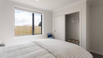 Een slaapkamer met een groot raam, een bed met gestreepte beddengoed, een kledingkast en een droogrek.
