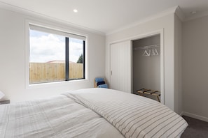 A bedroom with a large window, a bed with striped bedding, a wardrobe, and a drying rack.
