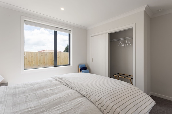 A bedroom with a large window, a bed with striped bedding, a wardrobe, and a drying rack.