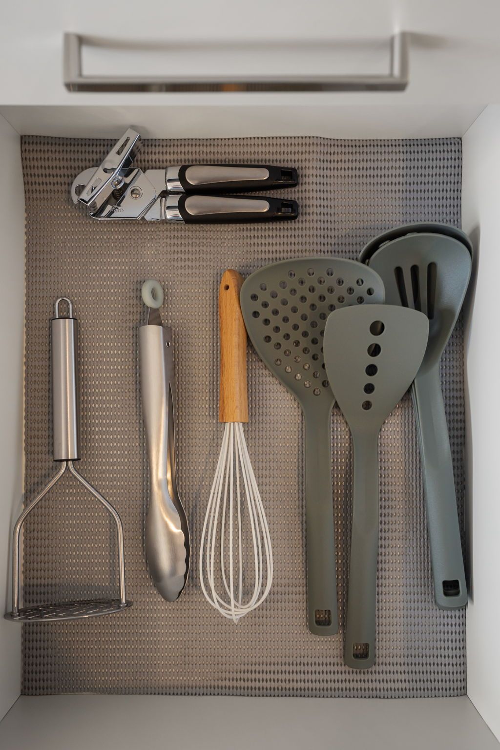 A kitchen drawer with various utensils including a whisk, spatulas, and a grater.
