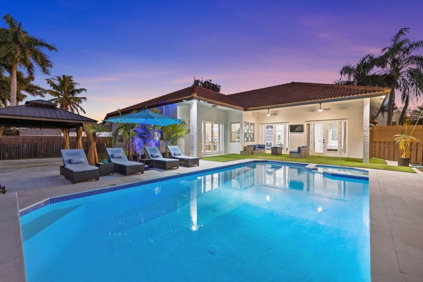 A residential swimming pool with lounge chairs and a covered patio area.