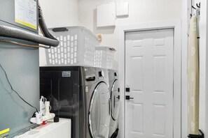 Uma lavanderia com duas máquinas de lavar, um secador e uma porta branca.