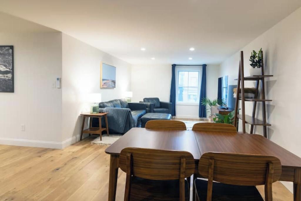 A dining area with a wooden table and chairs, a sofa, and a small side table with a lamp.