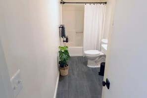Un baño pequeño con bañera, inodoro y una planta en maceta.