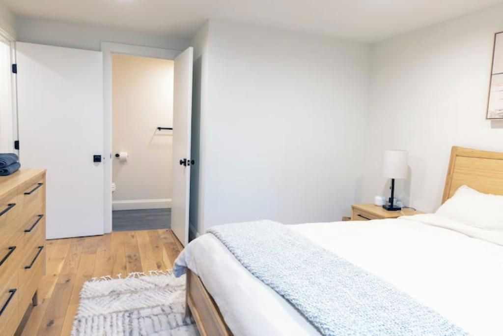 A bedroom with a bed, bedside table, lamp, and a door leading to another room.