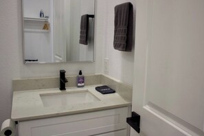 A bathroom with a white sink, a mirror, a towel rack, and a bottle of hand soap. - East Downtown Loft + Workspace (Houston)