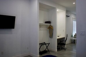 A room with a flat-screen TV mounted on the wall, a hanging coat rack, a foldable chair, and a small table with a potted plant. - East Downtown Loft + Workspace (Houston)