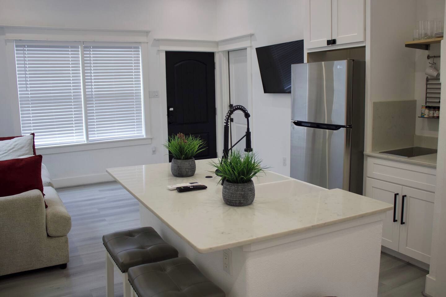 A modern kitchen with a central island, stainless steel appliances, and a flat-screen TV mounted above the island.