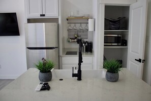 A modern kitchen with white cabinets, a stainless steel refrigerator, a microwave, and a coffee machine. There are two potted plants on the counter. - East Downtown Loft + Workspace (Houston)