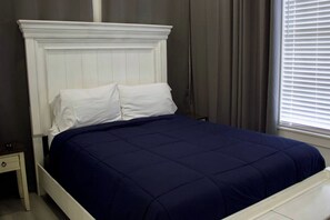 A bed with a white headboard and a dark blue bedspread in a room with a window and curtains. - East Downtown Loft + Workspace (Houston)