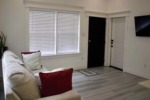 A living room with a sofa, red cushions, a door, and a wall-mounted television. - East Downtown Loft + Workspace (Houston)