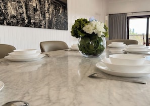 Ein Esszimmer ist gedeckt mit weißen Tellern und Schüsseln, eine Vase mit Blumen und ein Stadtbild-Wandgemälde an der Wand.