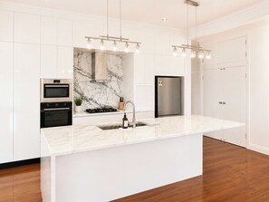 Ett modernt kök med vita skåp, en backsplash i marmor, rostfria vitvaror och hängande lampor.