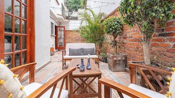 A patio with a sofa, wooden chairs, a table, and potted plants.