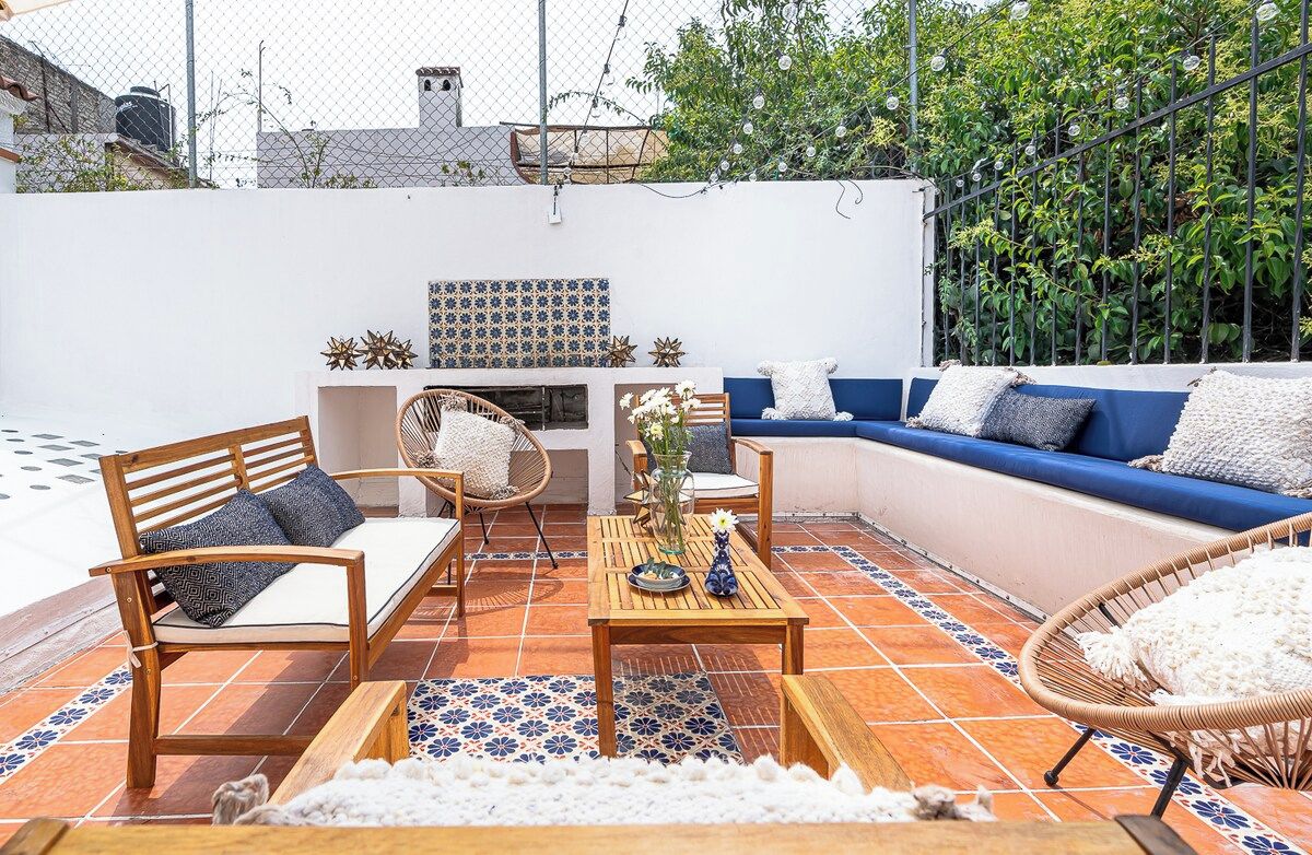 A patio with a blue sofa, wooden chairs, and a tiled floor.