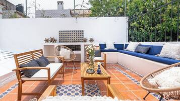 A patio with a blue sofa, wooden chairs, and a tiled floor.