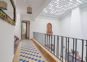 Un couloir avec un sol à carreaux, un escalier doté d’une rampe et un miroir décoratif.