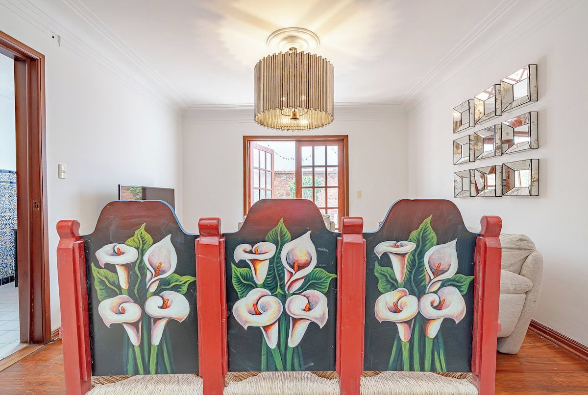 A hallway with a decorative wall panel featuring calla lilies, a chandelier, and a door leading outside.