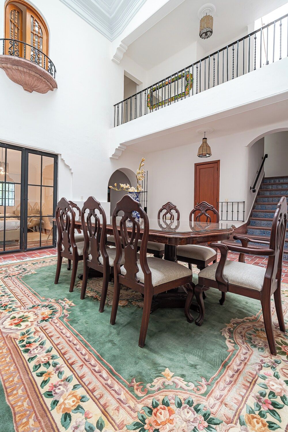 A spacious dining area with a high ceiling, a balcony, and a staircase.