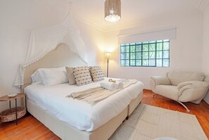 Une chambre à coucher avec un lit à baldaquin, une lampe de chevet, une chaise et une fenêtre ornée de barreaux en fer décoratifs.