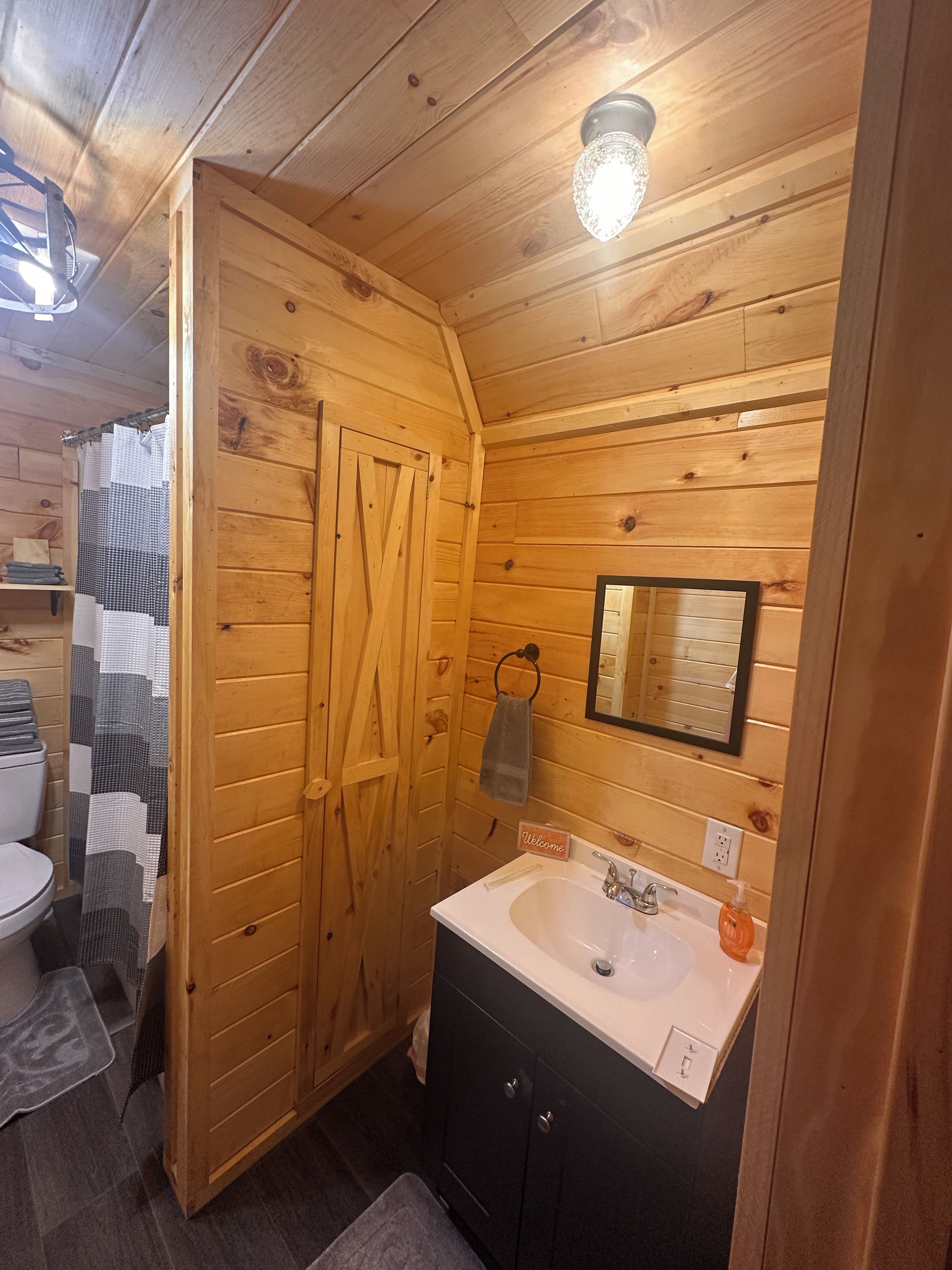 Un baño con paneles de madera, un lavamanos blanco, un perchero y un cartel de 'Welcome'.