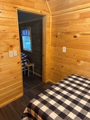 A wooden room with a bed, a chair, and a window.