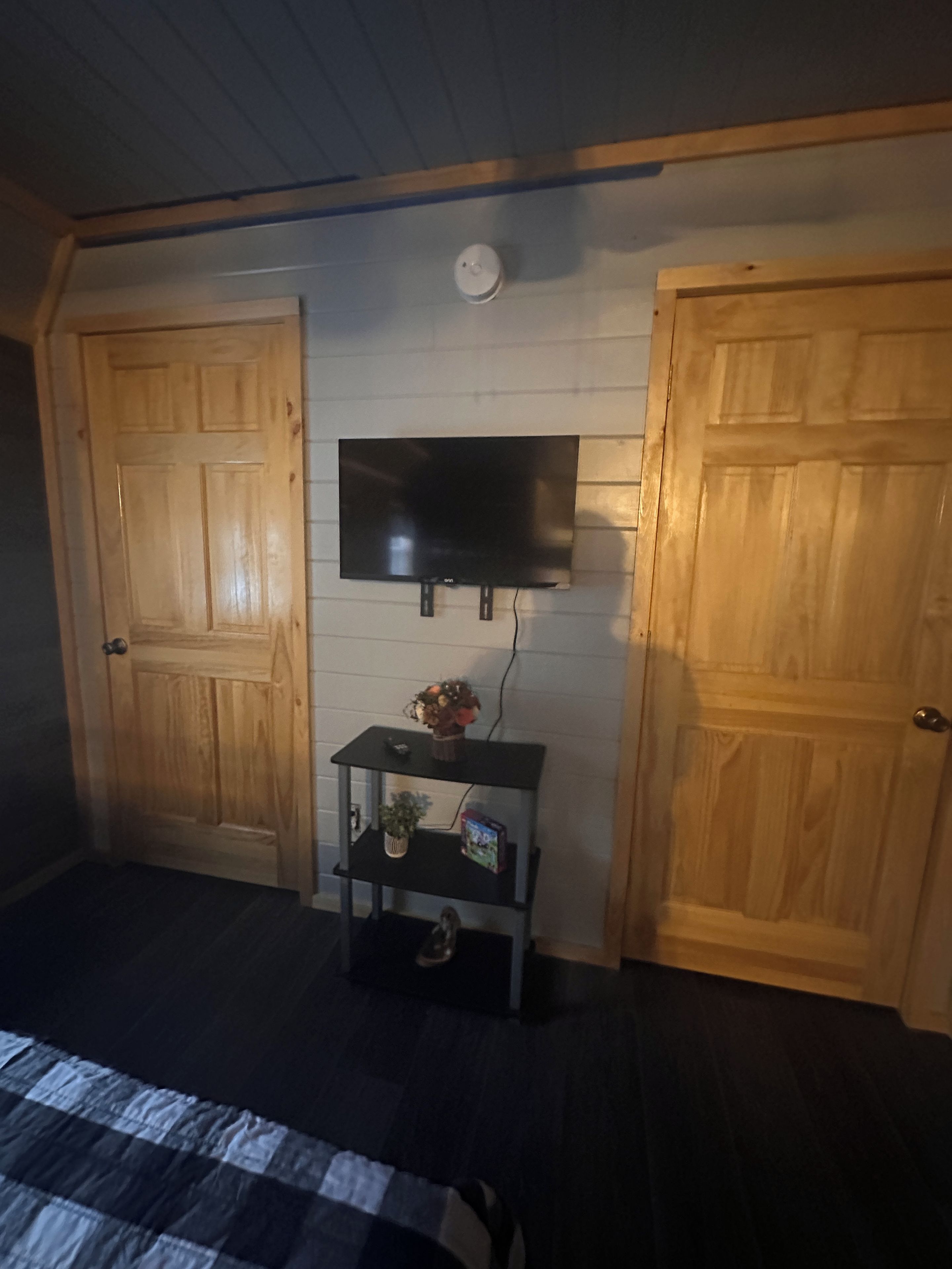 Een kamer met een bed, een aan de muur bevestigde televisie en twee houten deuren.