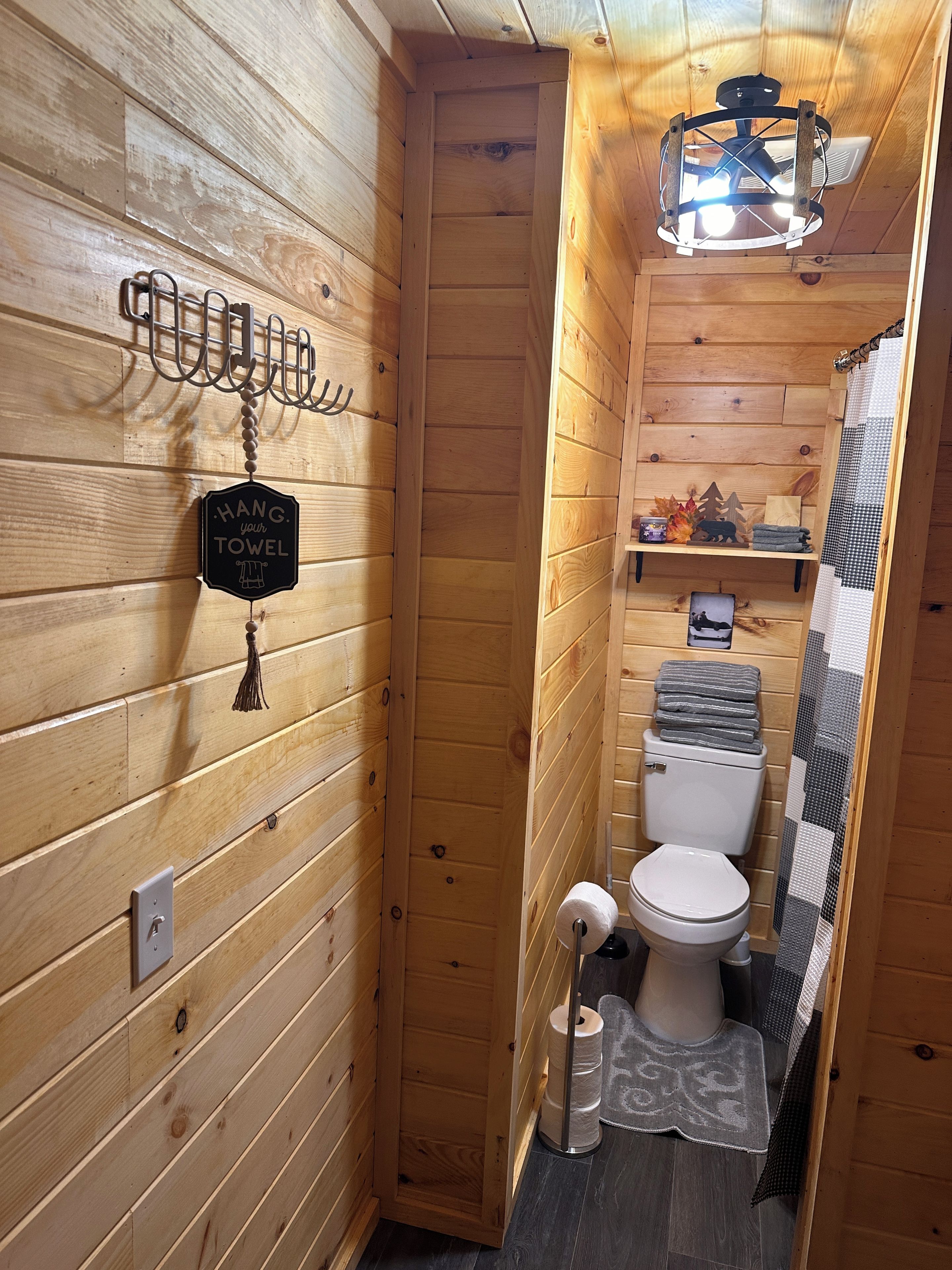 A wooden-paneled bathroom with a hanging towel rack, toilet, and a shelf with toiletries.