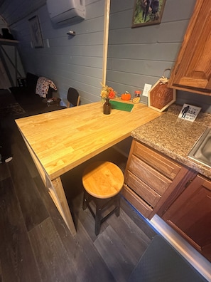 A kitchen with a wooden countertop, a stool, a vase with dried flowers, a pumpkin, and a sign with a quote.